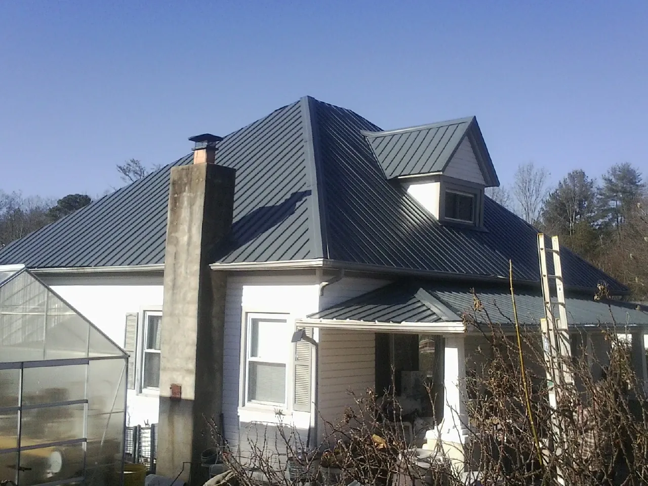 Dark blue standing seam metal roof on a white farmhouse with dormer — Slate & Tile Roof Repair by Roofing Brothers in Ten Sleep