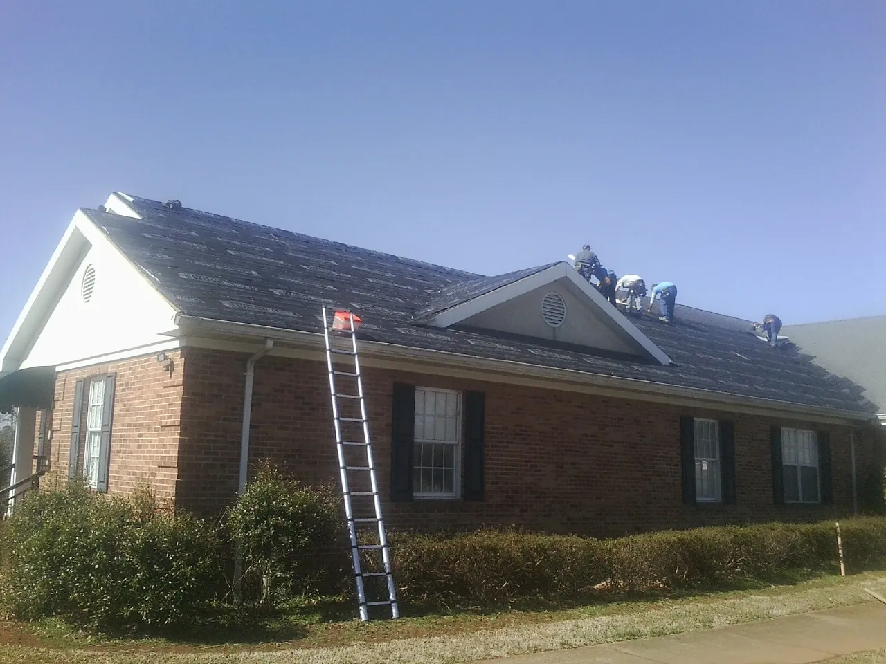 Crew tearing shingles off a brick ranch roof with a ladder set — Metal Roof Repair work by our crew in Ten Sleep
