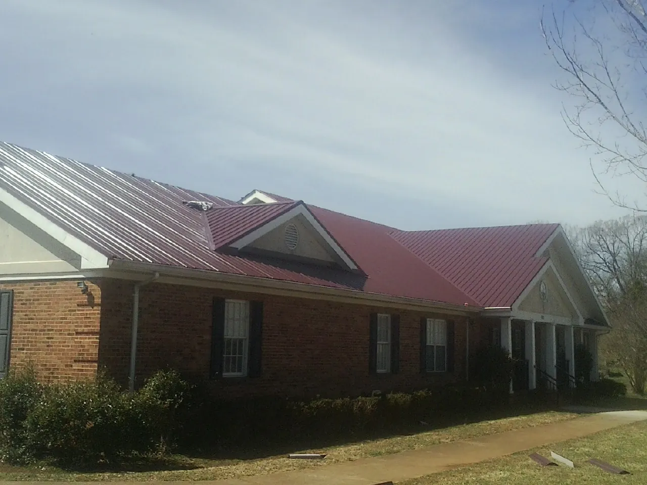 Red metal roof with gabled entries on a long brick building, from a Hail Damage Roof Repair job in Ten Sleep