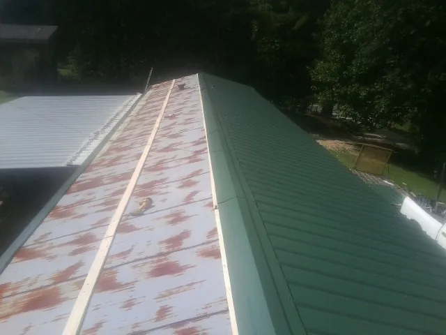 Old rusted panels beside newly installed green metal roofing — Wind Damage Roof Repair by Roofing Brothers in Ten Sleep