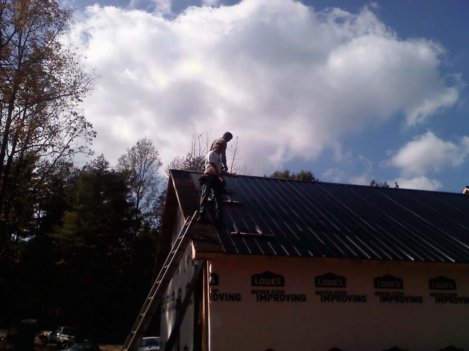 Roofer fastening dark metal panels high against a cloudy sky, from a Roof Inspection job in Ten Sleep