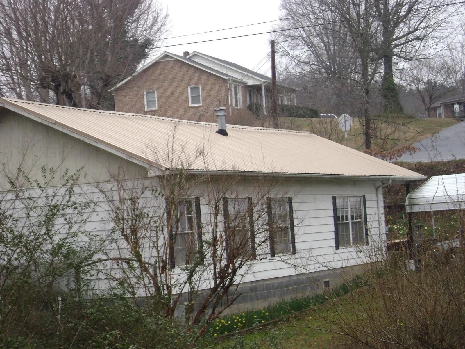 Tan metal roof on a white sided house set into a hillside — Commercial Roofing by Roofing Brothers in Ten Sleep