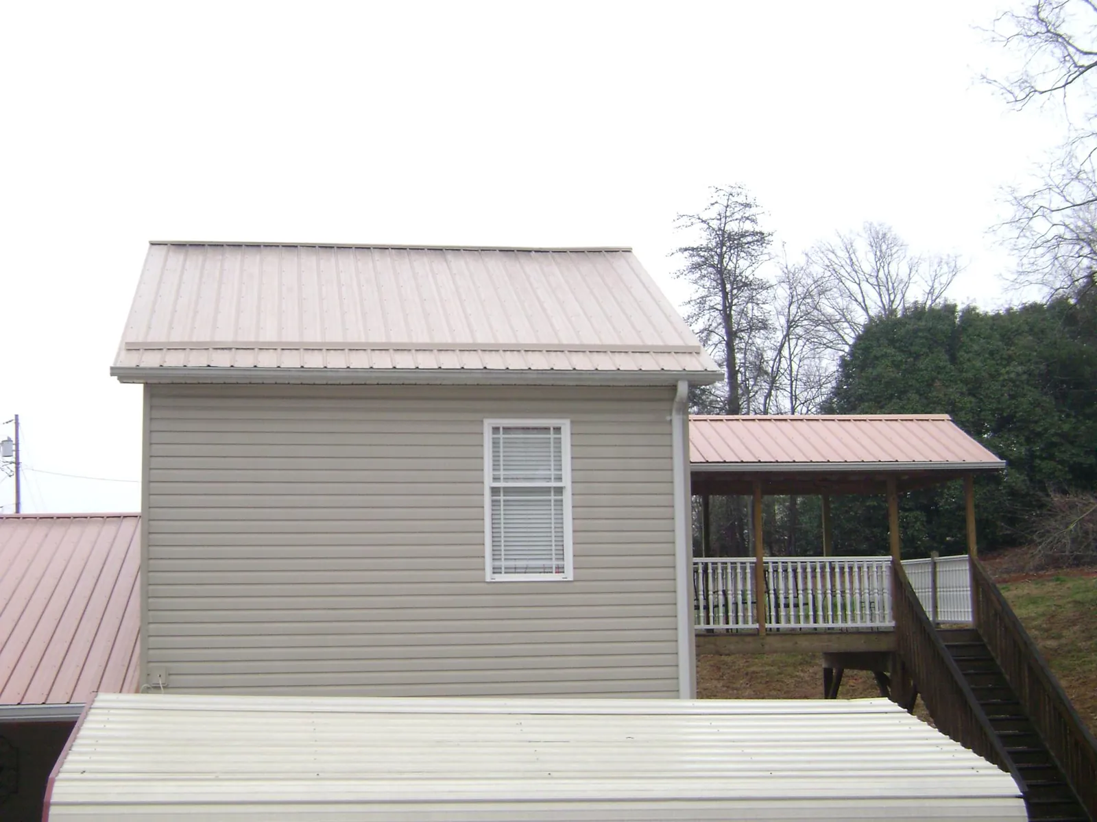 Tan metal roofs on a two story addition and attached porch, from a Roof Replacement job in Ten Sleep